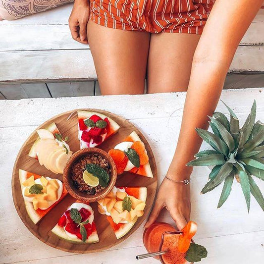Watermelon Pizza on wood plate with woman reaching for tropical juice drink, best vegan cookbook