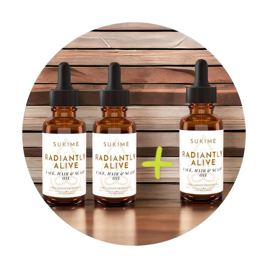 3 bottles of Sukime's Radiantly Alive natural face oil, vegan hair oil and scalp combined as one product. Sitting on wood table with wood wall behind. 