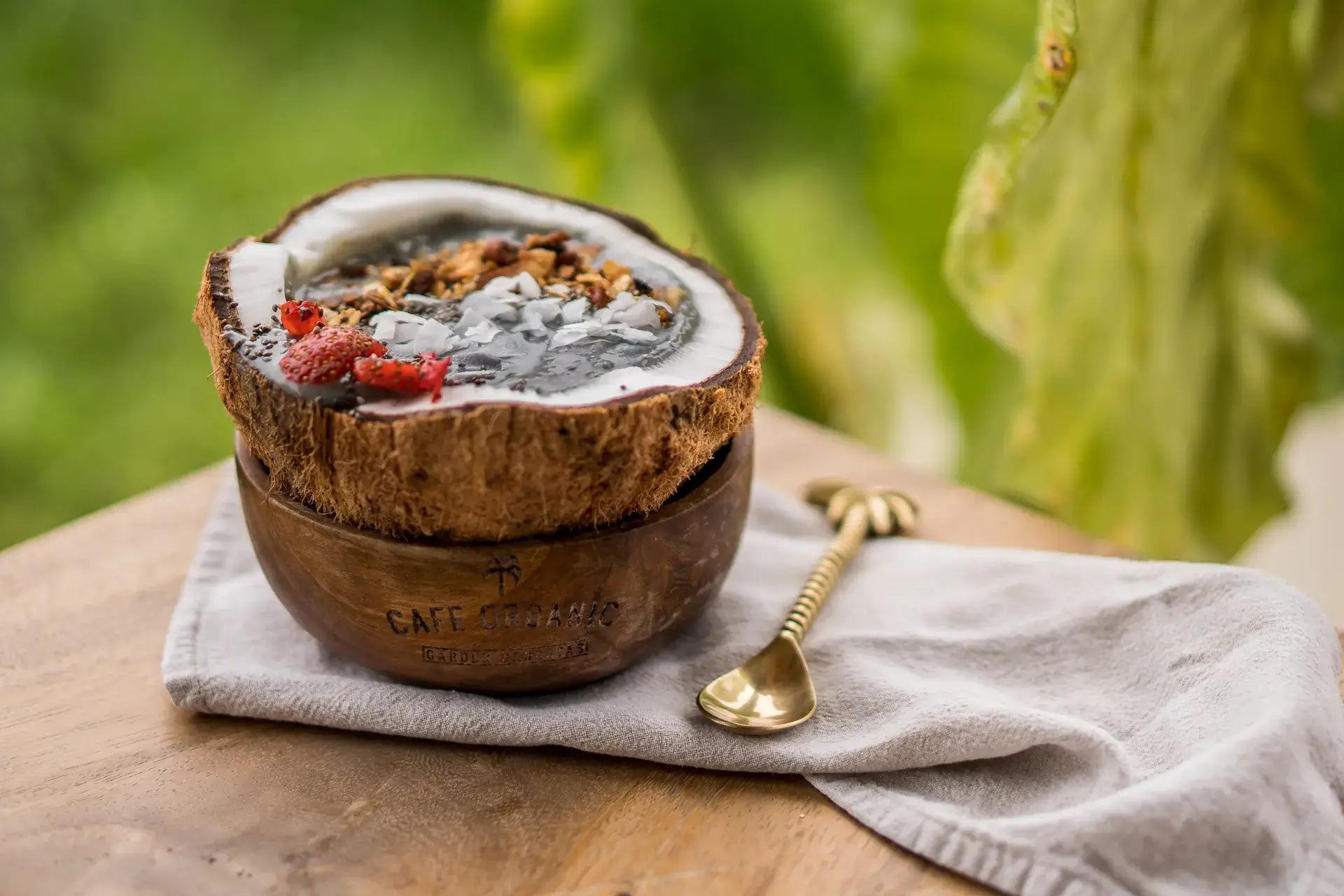 smoothie bowl inside a coconut on wood table with brass spoon from Bali Vegan Book